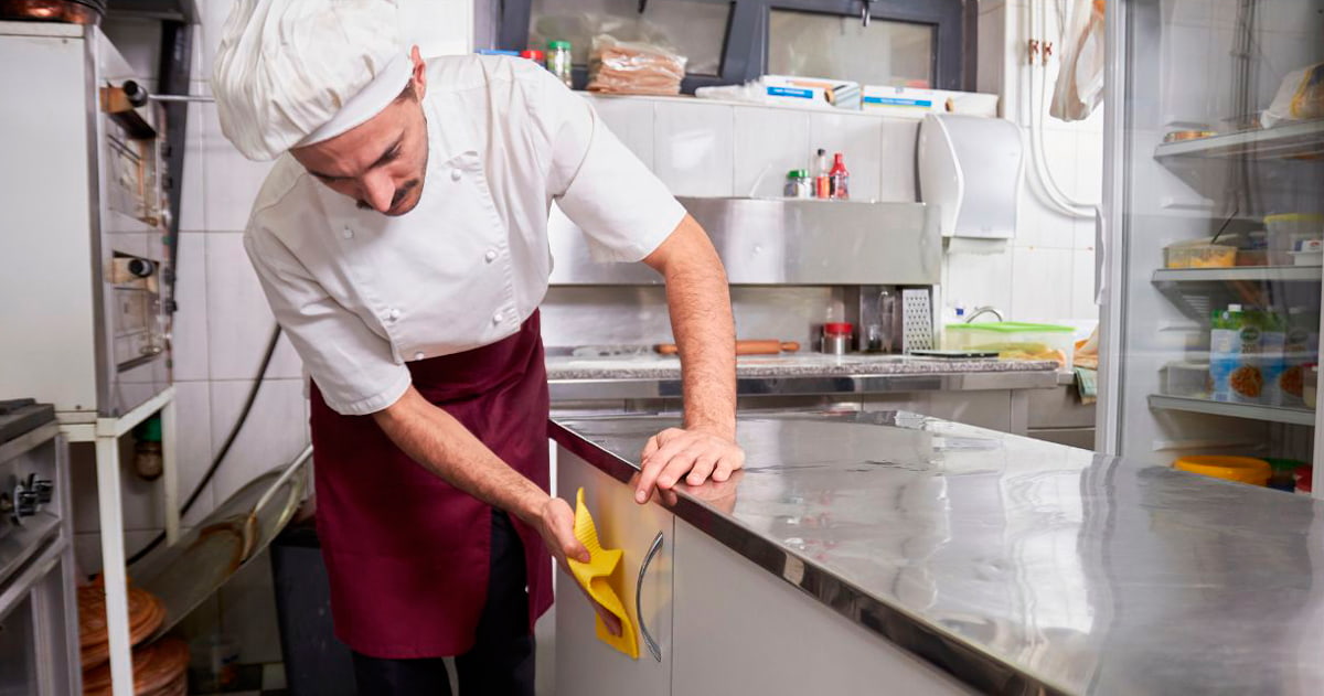 Operario aplicando detergente desinfectante profesional en superficie de cocina industrial